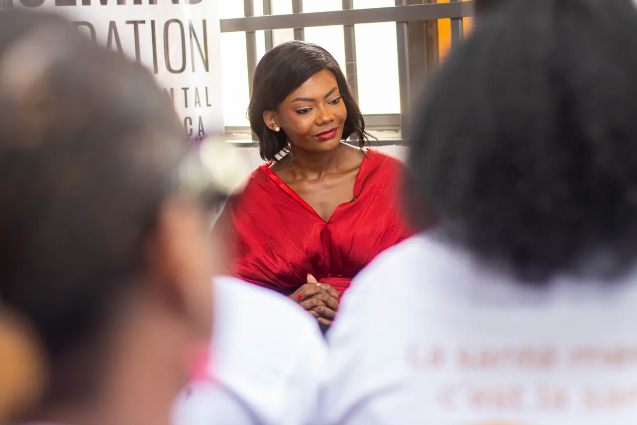 Marie-Alix de Putter in a red dress during a listening session in front of a Bluemind Foundation banner, surrounded by Heal by Hair ambassadors.