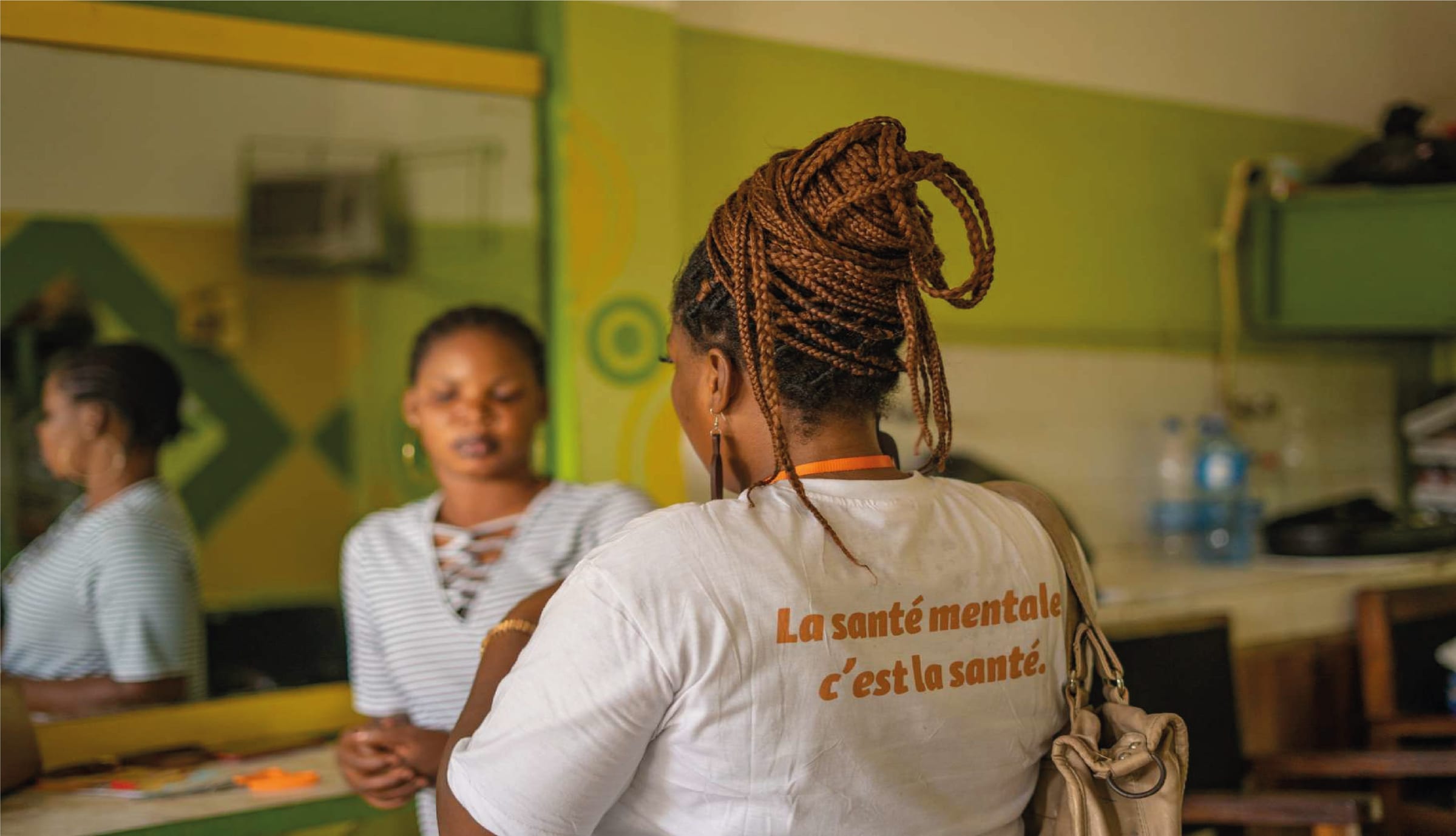 Woman from behind in a hair salon, braided updo, white T-shirt with the message: mental health is health